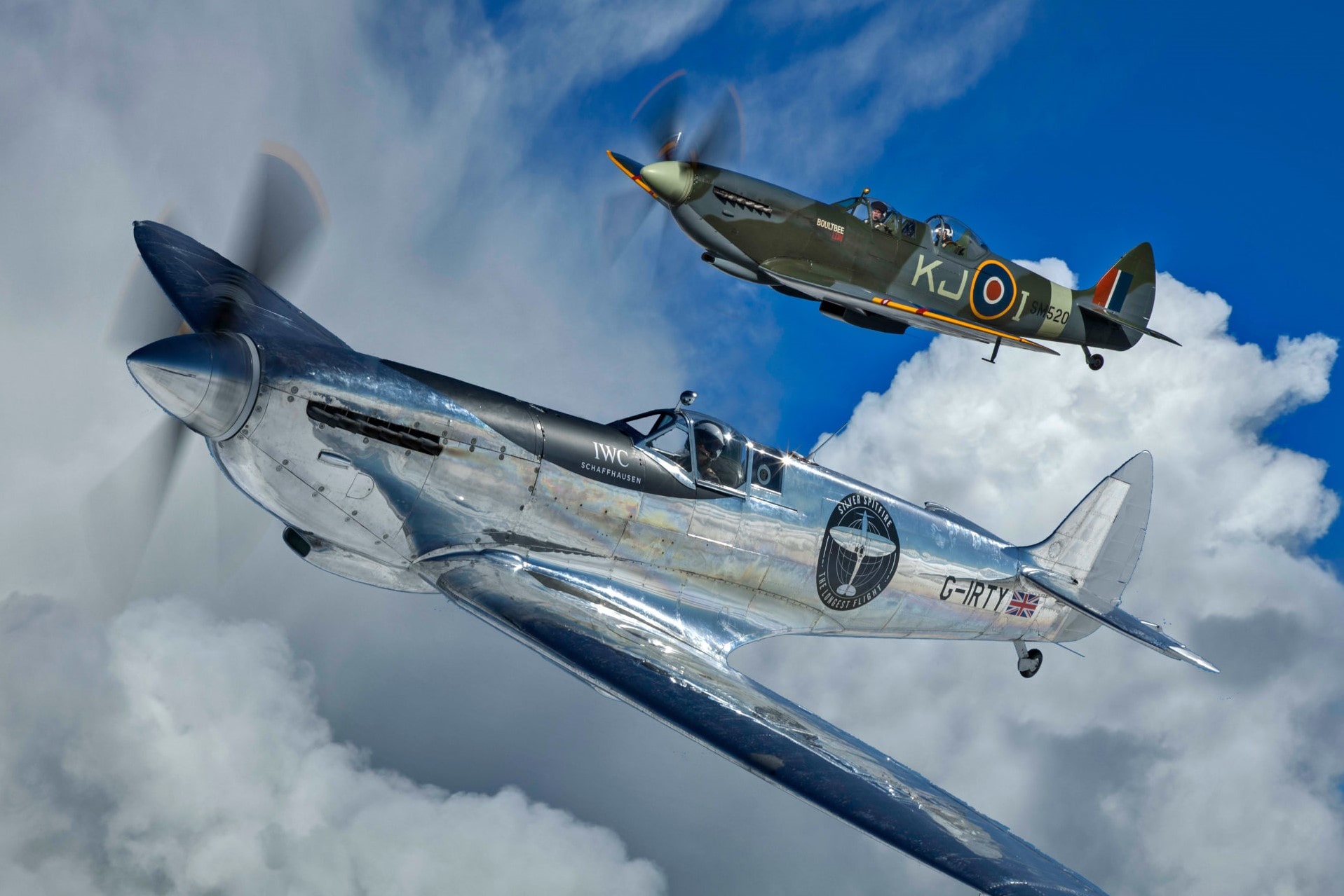 A silver spitfire flying alongside a classic Royal Airforce version in the clouds
